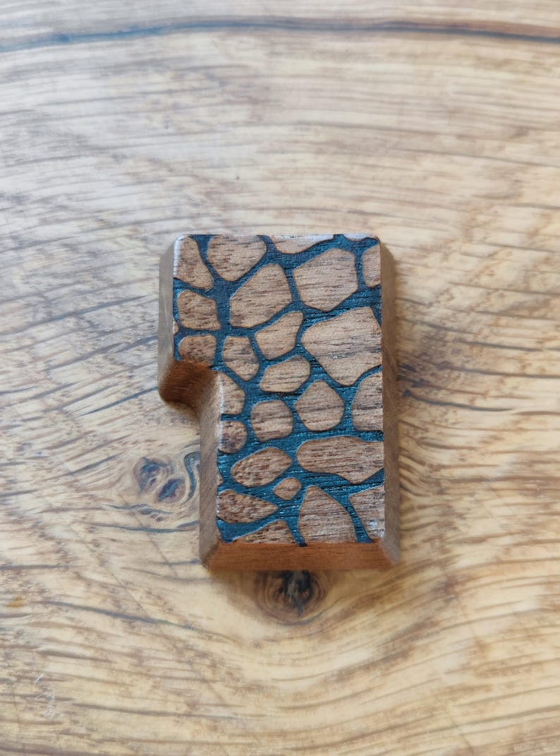 May include: A wooden keycap with a dark brown finish and a black geometric pattern.