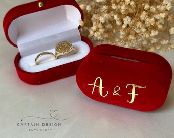 May include: Two red velvet ring boxes. One box has a gold ring and a gold ring with a green stone. The other box has the initials A & F in gold lettering.