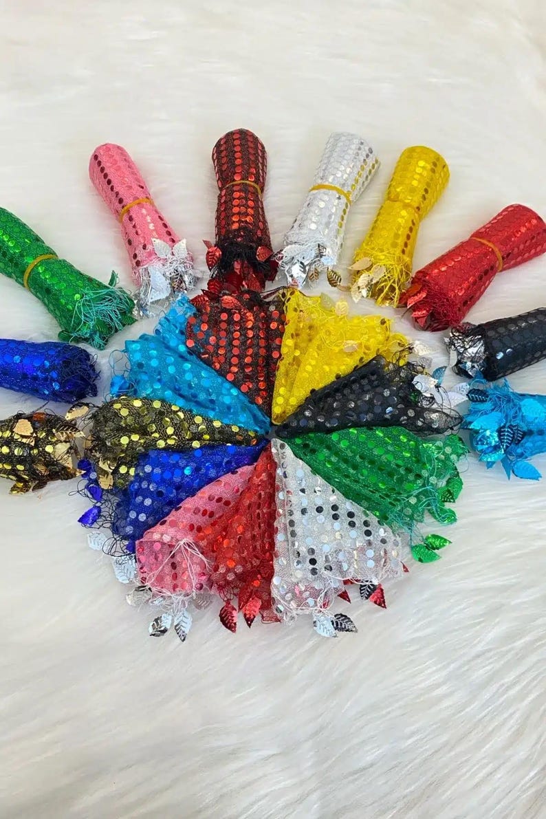 May include: A collection of colorful sequin fabric rolls and matching fan-shaped pieces. The rolls are in various colors, including pink, red, green, and gold. The fan pieces are arranged in a circle, showcasing the variety of colors and textures.