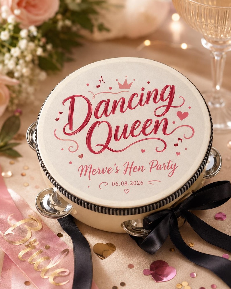 May include: A round tambourine with a cream-colored head featuring the red text Dancing Queen, Merve's Hen Party, and the date 06.08.2026. The design includes a small crown, musical notes, and hearts. A black ribbon is tied to the side frame.