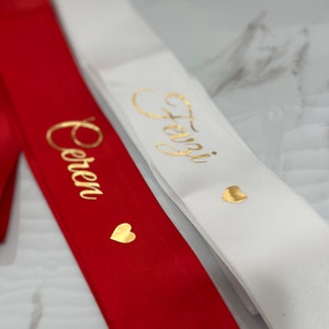 May include: Two satin sashes with gold lettering and hearts. The sash on the left is red with the word "Forever" in gold lettering. The sash on the right is white with the word "Always" in gold lettering.