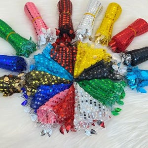 May include: A collection of colorful sequin fabric rolls and matching fan-shaped pieces. The rolls are in various colors, including pink, red, green, and gold, secured with elastic bands. The fan pieces are adorned with sequins and leaf-shaped embellishments.