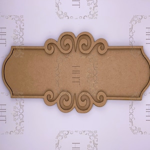 Könnte beinhalten: Ein Holzschild mit einem dekorativen Schriftrollen-Design. Das Schild ist leer und bereit, personalisiert zu werden.