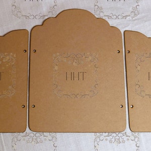 Puede incluir: Tres paneles de madera sin terminar con bordes festoneados y adornos decorativos. Los paneles están etiquetados con "HIHT" y tienen agujeros para colgar.