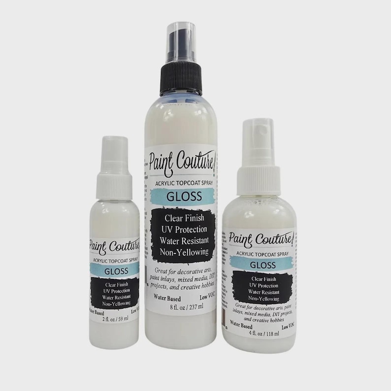 May include: Three white spray bottles of Paint Couture acrylic topcoat gloss. The bottles vary in size, with labels that include "Clear Finish", "UV Protection", and "Water Resistant". The largest bottle contains 237 ml.