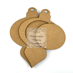 Op de afbeelding: Ongafgewerkte houten kerstornamentuitsparingen in verschillende vormen, waaronder een druppel, een cirkel en een ovaal. De ornamenten zijn gelaagd en hebben een klein gaatje aan de bovenkant om op te hangen. De tekst "Handcrafted Holiday Traditions" is zichtbaar.