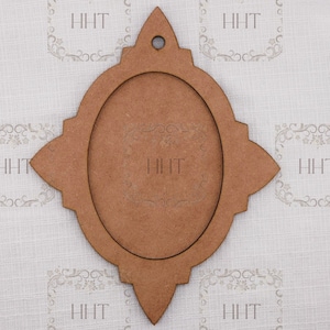 May include: A brown wooden frame with an oval opening and decorative edges. The frame has a hole at the top for hanging and the letters "HHT" are visible. The frame is designed for displaying photos or artwork.
