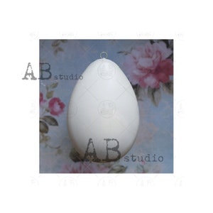 May include: A large, white egg-shaped ornament with a small metal loop at the top for hanging. The ornament has a smooth surface and is likely made of a lightweight material. The background features a floral pattern with pink and red flowers.