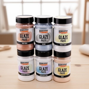 May include: Six jars of Pentart Glaze Paste arranged in two rows of three. The labels feature the text GLAZE PASTE and color names: Rose Gold, Silver, Pearl White, Iridescent Purple, Iridescent Blue, and Gold. Each jar has a black screw-top lid.