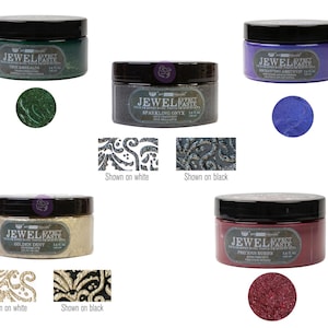 Puede incluir: Cuatro frascos de pasta Jewel Effect en diferentes colores: esmeralda, ónix, polvo dorado y rubíes preciosos. Cada frasco tiene una tapa negra y una etiqueta con el nombre del producto y el color. La pasta se muestra sobre fondos blanco y negro.