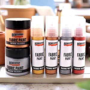 Könnte beinhalten: Ein Set mit sechs metallischen Textilfarben in Gold, Kupfer, Silber, Grau und Rot. Die Farbflaschen sind mit "Pentart Fabric Paint" und "Machine Washable" beschriftet.