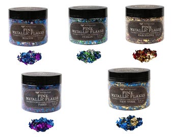 May include: Five jars of fine metallic flakes, each with a different city name: Moscow, Dublin, Barcelona, Paris, and New York. Each jar contains a variety of metallic flakes in different colors and sizes.