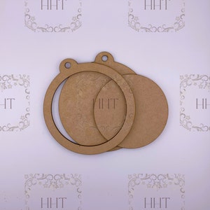 May include: A collection of unfinished wooden ornaments, including circular frames and solid circles. Each ornament has a natural wood tone and a small hole for hanging. The letters "HHT" are visible on some of the ornaments.