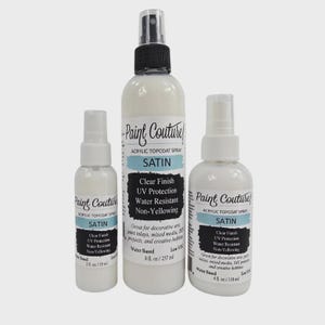 May include: Three white Paint Couture Acrylic Topcoat Satin spray bottles. The bottles have black and blue labels with text including "Clear Finish", "UV Protection", and "Water Resistant". Sizes include 59 ml, 237 ml, and 118 ml.
