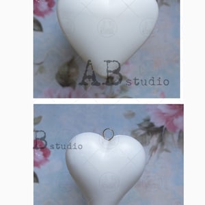 Könnte beinhalten: Zwei weiße herzförmige Ornamente mit goldenen Oberteilen. Die Ornamente hängen an einer Schnur und befinden sich vor einem hellblauen Hintergrund mit rosa Blumen.