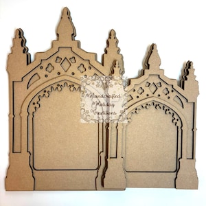 May include: Two unfinished wooden arch-shaped frames with intricate cut-out designs. The frames feature pointed tops and decorative details, with the text "Handcrafted Holiday Traditions" visible. The frames are designed to stand upright.