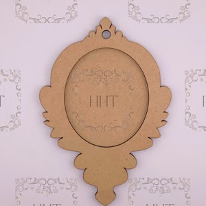 Op de afbeelding: Een houten fotolijst met een sierlijk ontwerp. De lijst is bruin en heeft een ronde opening in het midden. De lijst is versierd met een bloemmotief.