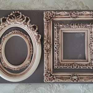 May include: Two ornate picture frame molds. One is oval-shaped with a crown design, the other is rectangular. Both frames have a cream and brown color scheme and are set against a gray background.
