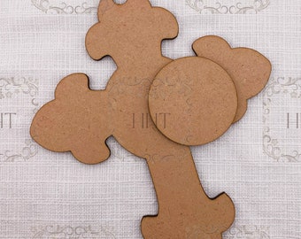 May include: Three unfinished wooden craft pieces: a cross, a circle, and a smaller cross shape. The pieces are arranged on a textured fabric background.