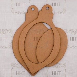 Op de afbeelding: Een stapel van drie onafgewerkte houten kerstornamenten. De ornamenten hebben de vorm van een druppel met een lus aan de bovenkant om op te hangen. Het hout heeft een lichtbruine kleur en een glad oppervlak. De letters "HHT" zijn vaag zichtbaar.