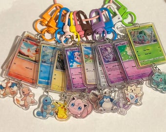 May include: A collection of rectangular clear acrylic keychains, each housing a trading card featuring various colorful cartoon creatures. Each keychain is attached to a vibrant plastic lobster clasp and includes a small acrylic charm.