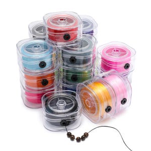 May include: A collection of multiple square, clear plastic spools containing vibrant colored elastic cord. Each spool features a black circular outlet for the thread. A single black cord extends from one spool, threaded with five small brown beads.