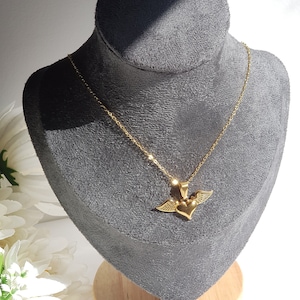 May include: Gold chain necklace with a heart pendant featuring wings. The heart is a 3D design and the wings are spread out.