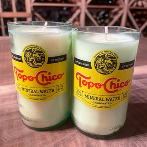 May include: Two glass bottles with green tops and yellow labels. The labels say "Topo Chico" and "Mineral Water Carbonated" with the text "Monterrey, Mexico".