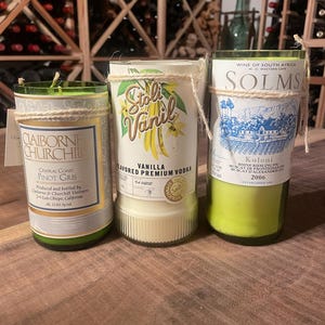 以下が含まれることがあります： ラベルが付いたガラス製のキャンドルジャーが3つあります。最初のジャーは緑色で、「Claiborne Churchill Central Coast Pinot Gris」と書いてあります。2番目のジャーは透明で、「Stoli Vanil Vanilla Flavored Premium Vodka」と書いてあります。3番目のジャーは緑色で、「Solms Koloni Rhine Riesling Spätlese Muscat de Frontignan Muscat d'Alexandrie 2006」と書いてあります。