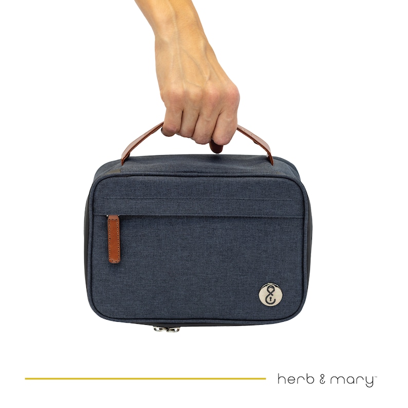 Może przedstawiać: Czarna, pł&oacute;cienna torba podr&oacute;żna z brązowym sk&oacute;rzanym uchwytem i zamkiem błyskawicznym. Torba ma małe, okrągłe logo z literami "&" w środku.