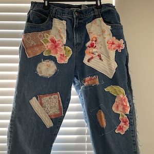 May include: Blue denim jeans with various fabric patches, including floral patterns, a vintage illustration of a woman, and paisley designs.