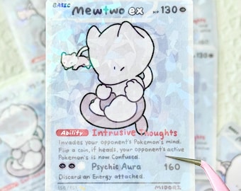 May include: A holographic Mewtwo ex Pokémon trading card. The card features a white Mewtwo illustration with black outlines, set against a light blue background. Text includes "Intrusive Thoughts" and "Psychic Aura".