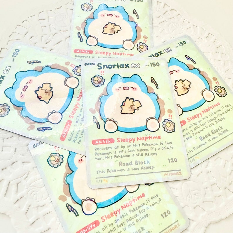 May include: A Snorlax Pokemon card with a light blue background and a cartoon illustration of Snorlax sleeping. The card has the text "Snorlax ex" and "Sleepy Naptime" on it. The card is 150 HP and has a Road Block ability.