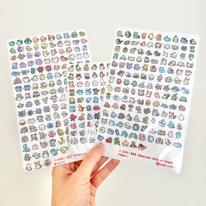 Może przedstawiać: Trzy arkusze papieru z naklejkami Pokemon z ilustracjami postaci Pokemon z region&oacute;w Kanto, Johto i Hoenn. Arkusze naklejek są oznaczone nazwą regionu i numerami Pokemon&oacute;w. Arkusze naklejek znajdują się na białym tle.