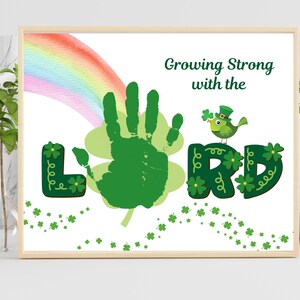 Może przedstawiać: Oprawiony wydruk z motywem Dnia Świętego Patryka. Grafika przedstawia zielony odcisk dłoni, tęczę oraz słowa "Growing Strong with the LORD". Zielony ptak w kapeluszu siedzi na słowie "LORD".