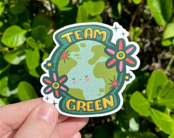 May include: A green and yellow sticker with the text "Team Green" and a cartoon earth with flowers. The earth has a smiling face.