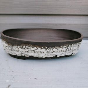 May include: An oval ceramic bowl with a smooth, dark brown interior and a textured, white, craggy exterior finish. The rim is dark brown, and the base is dark brown. The text MK Pottery is printed in white in the bottom left corner.