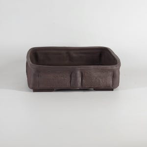 May include: A dark brown rectangular bonsai pot with a textured finish. The pot has a raised rim and is supported by four small feet. The shape is a long rectangle, ideal for bonsai trees. Measurements are in cm.