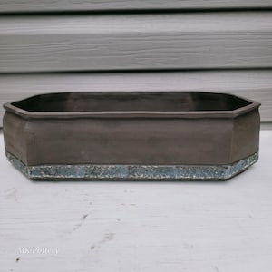 May include: A rectangular, low-profile ceramic bonsai pot with an octagonal shape. The main body is a matte dark brown, while the base features a textured, mottled blue and grey glaze. The text MK Pottery is printed in the bottom left corner.
