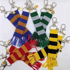 May include: A collection of keyrings with woven fabric strips in colours such as blue and gold, green and white, red and gold, and yellow and black. Each keyring has a silver clasp and a star charm, with fringed ends. Ideal for fans of a famous wizarding franchise.
