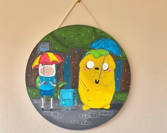May include: A round, black and white painted canvas with a scene of Finn the Human and Jake the Dog from Adventure Time. Finn is wearing a blue shirt and holding a red and yellow umbrella. Jake is a yellow dog wearing a blue umbrella and holding a green backpack. The background is a green forest with rain falling.