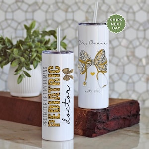May include: Two white insulated tumblers with straws. One features the text "PROTECTOR OF TINY HUMANS PEDIATRIC doctor" in leopard print and black script. The other has a bow, stethoscope, and the name "Dr. Omani" with "est. 2026".