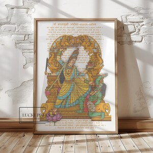May include: Framed artwork featuring a colorful illustration of a deity with multiple arms, set against a backdrop of script. The artwork is in a wooden frame and is displayed on a wooden floor.