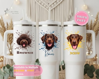 May include: Three white stainless steel tumblers with handles and straws. Each features a dog portrait with a colorful paint splatter design and a name printed below: Brownie, Ronni, and Jackson. The tumblers have a smooth finish.