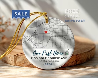 May include: A round white ceramic ornament featuring a black and gray street map with a red heart icon. The text reads Our First Home, 1155 GOLF COURSE AVE, Santa rosa, CA, and 2026. It includes a gold hanging cord and a small house illustration.
