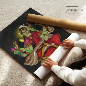 May include: A colorful painting of a Hindu goddess playing a stringed instrument, a veena, with four arms. She is wearing a red and gold sari and has a green complexion. The painting is on a black background and has a gold border. The text "LUCKY PIXELS 28 ART STUDIO" is in the upper right corner.