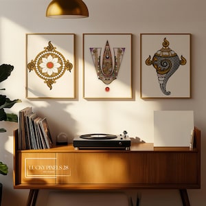 May include: Three framed art prints with gold frames. The prints feature intricate, colorful designs on a cream background. A wooden cabinet with a record player and records is below the prints. The text "LUCKY PIXELS 28 ART STUDIO" is on the cabinet.