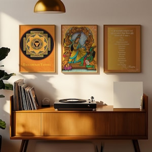 May include: Three framed prints on a wall above a wooden shelf with a record player and a stack of vinyl records. The prints are all gold-toned and feature images of Hindu deities and symbols. The text on the rightmost print reads "If all religious writings are  put to the test by the fire of  reason, only the true ones will  remain.  - Mahatma Gandhi"