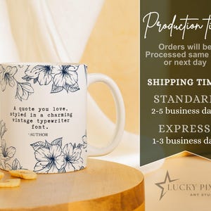 May include: A white ceramic mug featuring a dark blue floral pattern and the printed text: A quote you love, styled in a charming vintage typewriter font. -AUTHOR. The mug has a curved handle and is positioned on a smooth, rounded wooden surface.