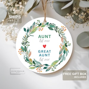 May include: A round white ornament with a watercolor floral wreath design. The text reads "AUNT Est. 2022" and "GREAT AUNT Est. 2025" with a red heart in between. The ornament hangs from a natural twine string.